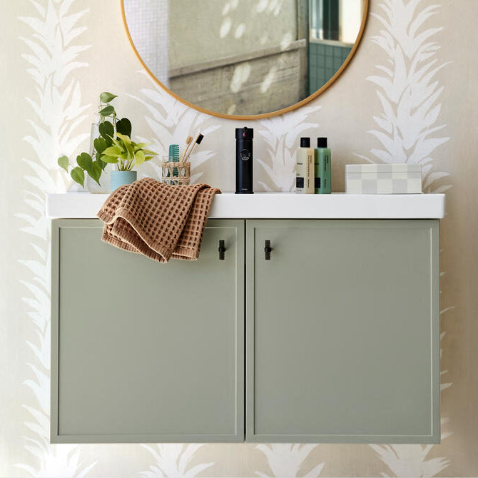 smoke acrylic and matte black stem knobs installed on pale green bathroom vanity cabinet