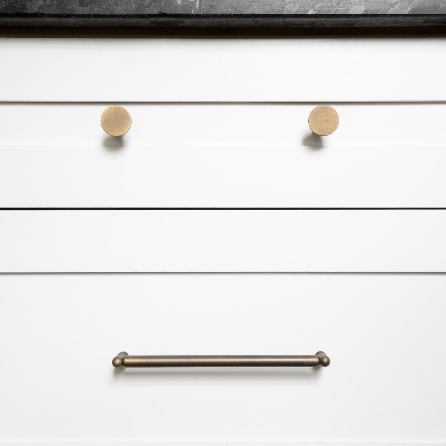 Close-up of white drawers with antique english knobs and an antique english handle.