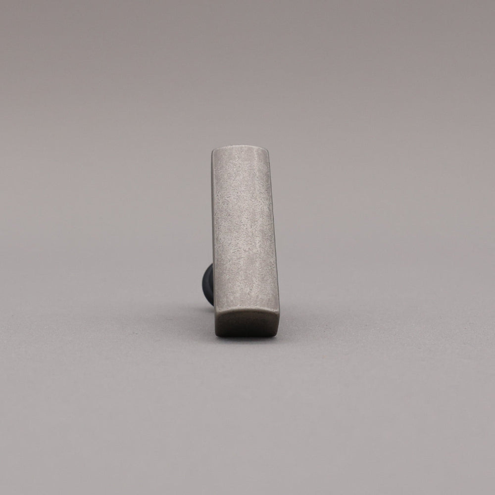 Front leaning matte black and weathered nickel t-knob brass cabinet knob on gray background.