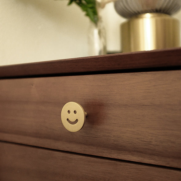 Close-up of Satin Brass Smiley Knob installed on a brown side-table drawer