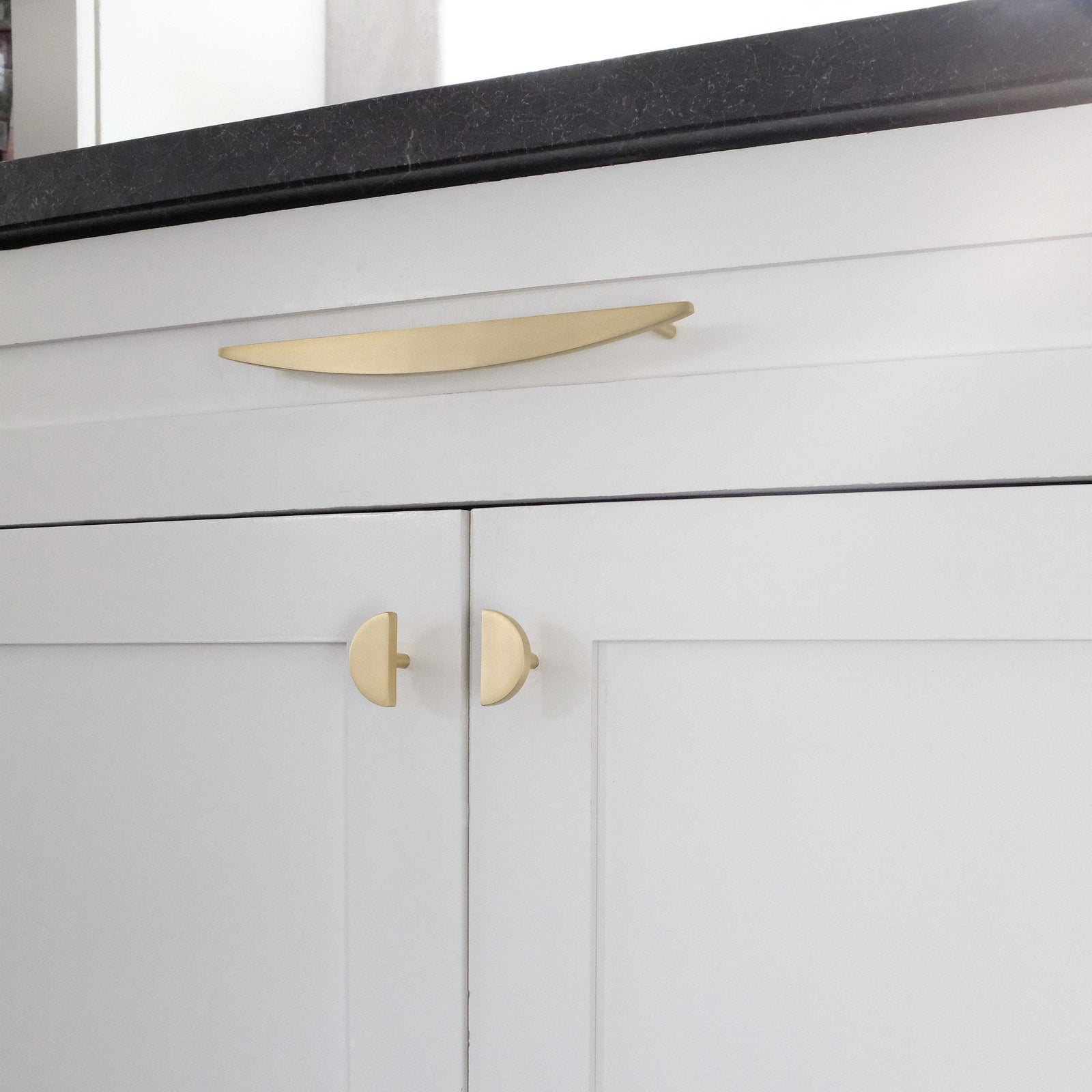 Gold cabinet knobs mixed with gold cabinet pull on white kitchen cabinets with black counter