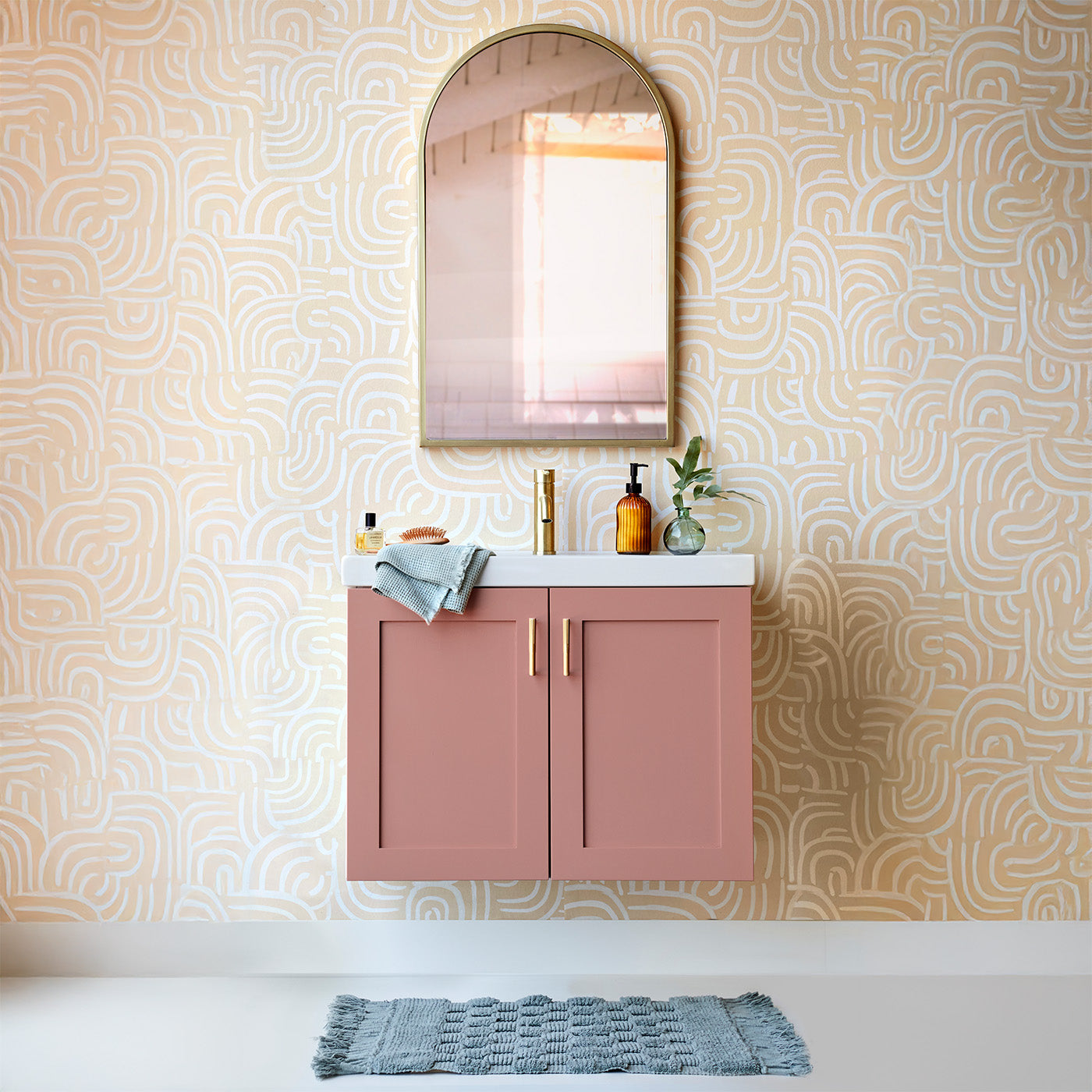 Pink bathroom vanity with orange wallpaper and floating vanity with satin brass hardware and fauce and mirror.