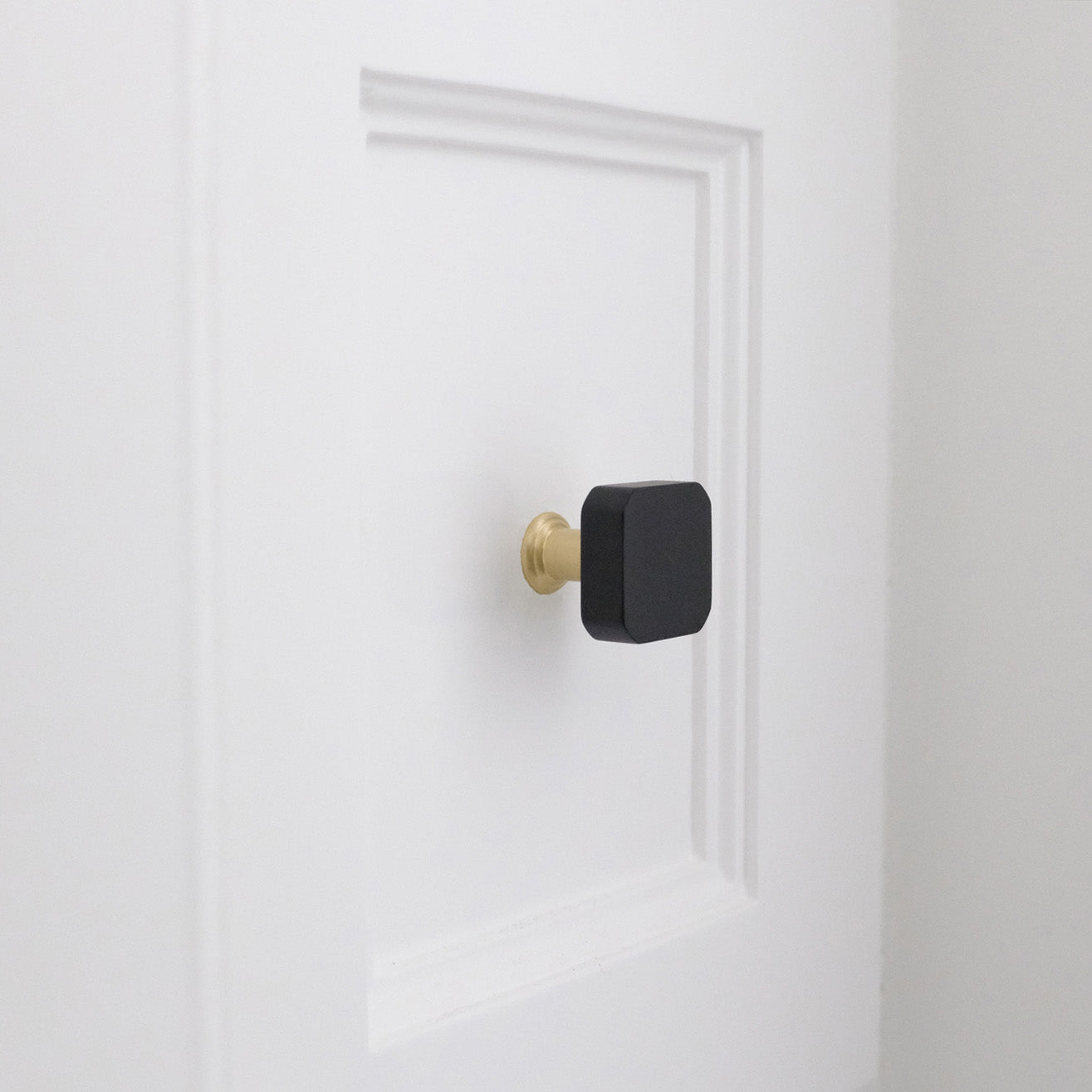 Two tone satin brass and matte black knob on a white shaker drawer in a bathroom.