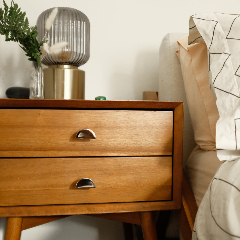 Polished nickel dresser drawer knobs on wooden drawers and a gold lamp