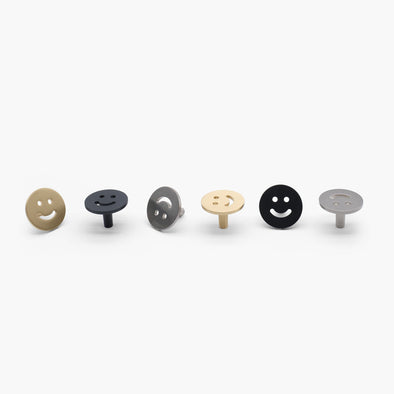 Six Hapny Smiley knobs facing different directions and in three finishes - Satin Brass, Satin Nickel, and Matte Black.