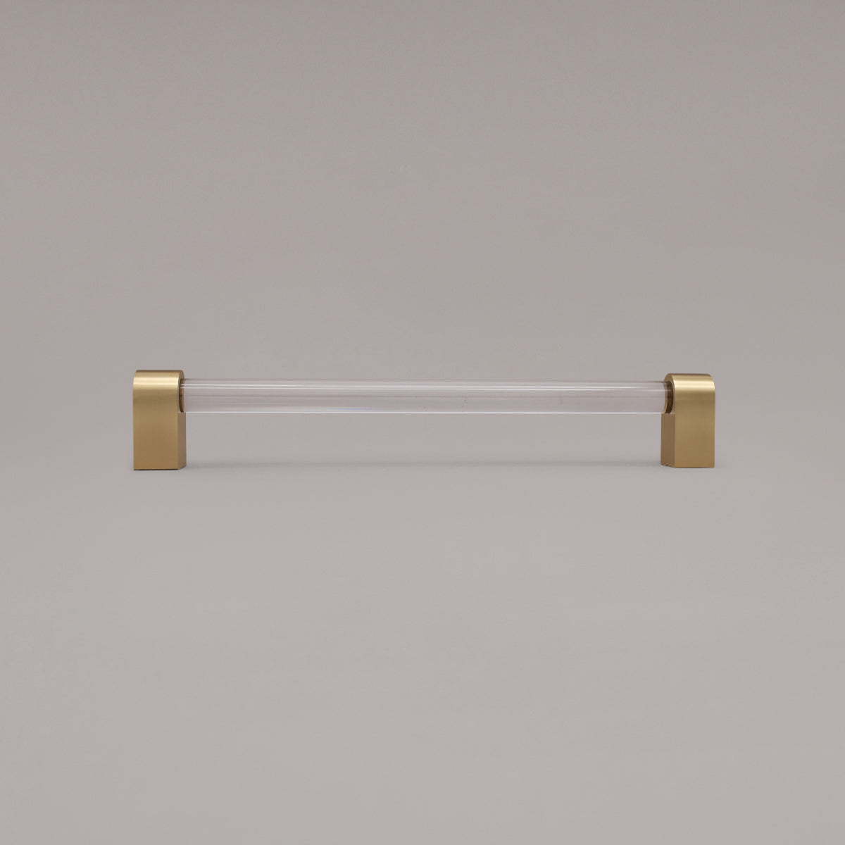 Clarity clear acrylic and satin brass stems 12 inch appliance pull standing on gray background