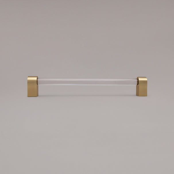 Clarity clear acrylic and satin brass stems 12 inch appliance pull standing on gray background