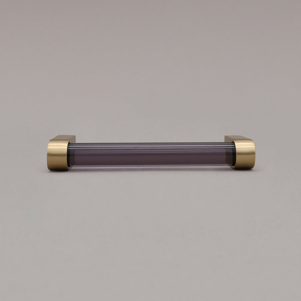 small smoke and satin brass cabinet pull laying on gray background