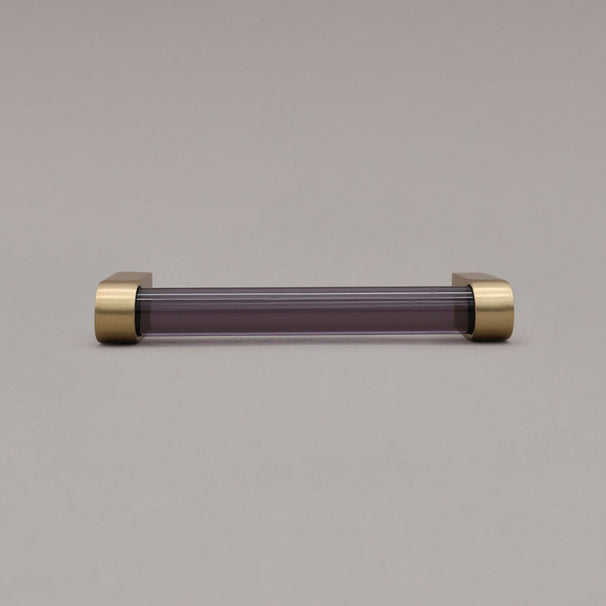 small smoke and satin brass cabinet pull laying on gray background