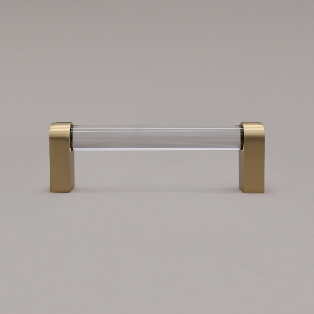 small clear and satin brass cabinet pull standing on gray background