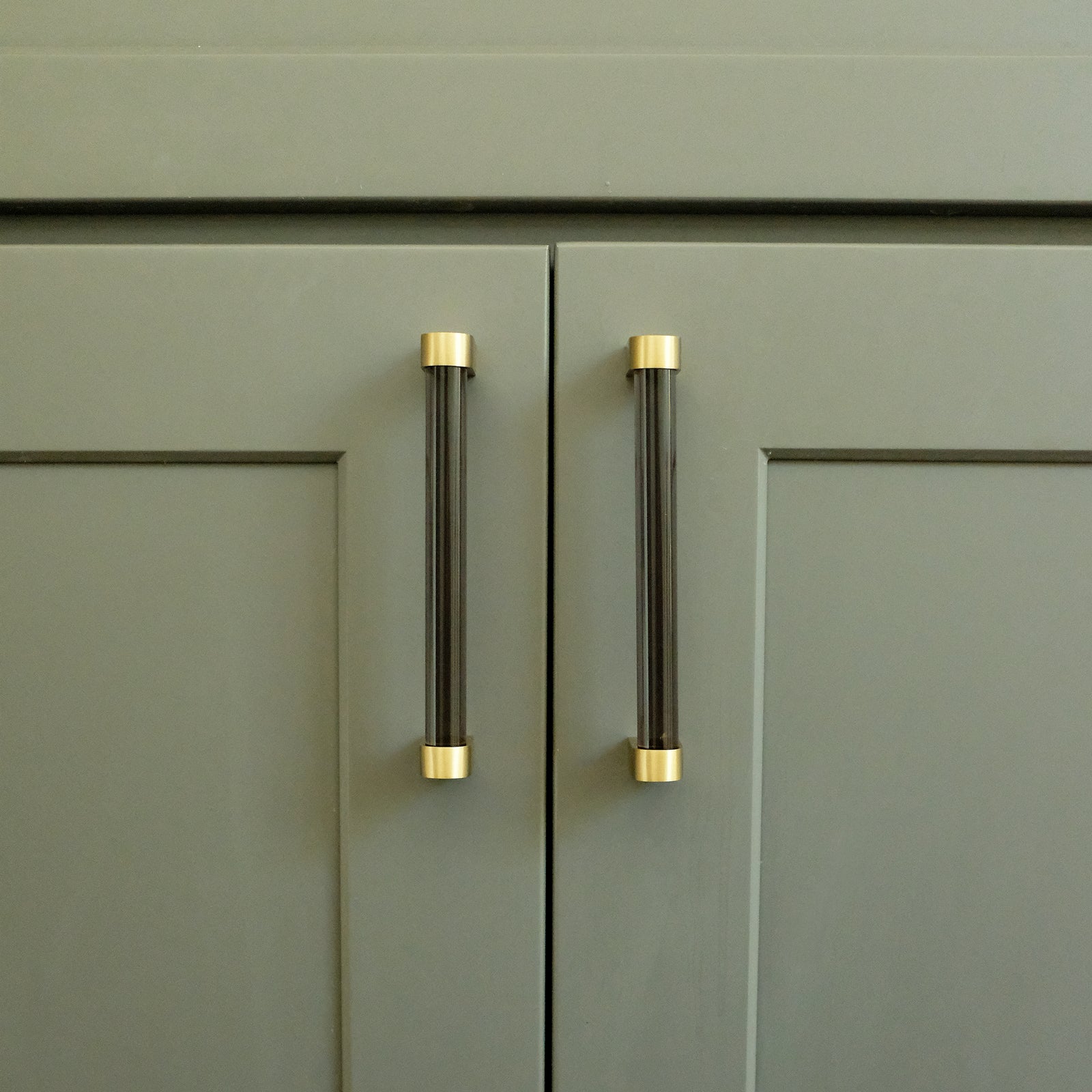 Two smoke acrylic pulls with gold accents on bathroom vanity cabinet doors. 