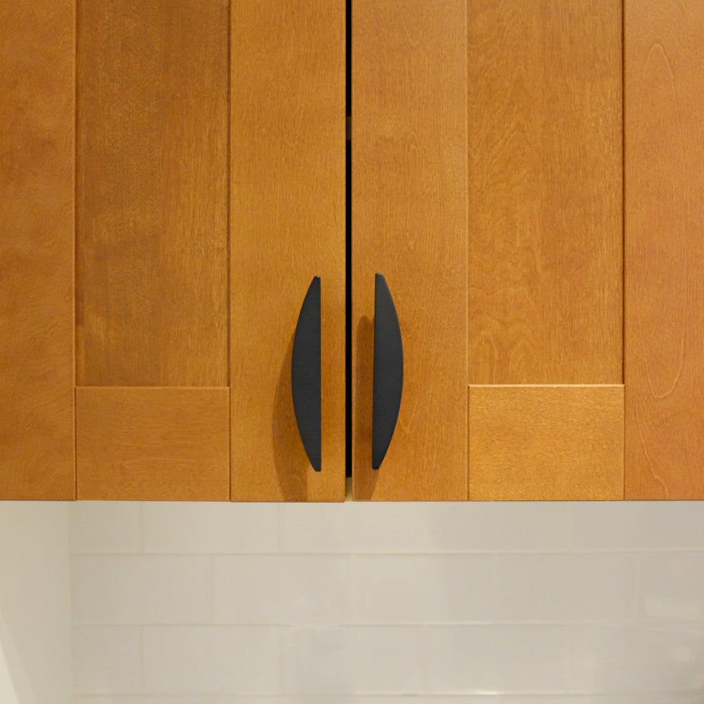 Two matte black half moon pulls installed on warm wood cabinet