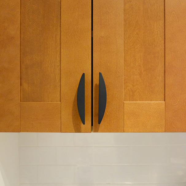 Two matte black half moon pulls installed on warm wood cabinet