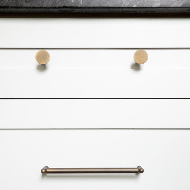 Knurled antique english cabinet knobs and cabinet pull installed on white kitchen drawers with black marble countertop 