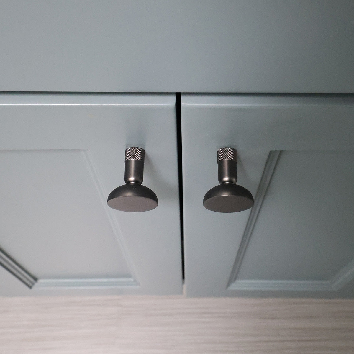 Close-up of two graphite knurled cabinet knobs on blue bathroom cabinets.