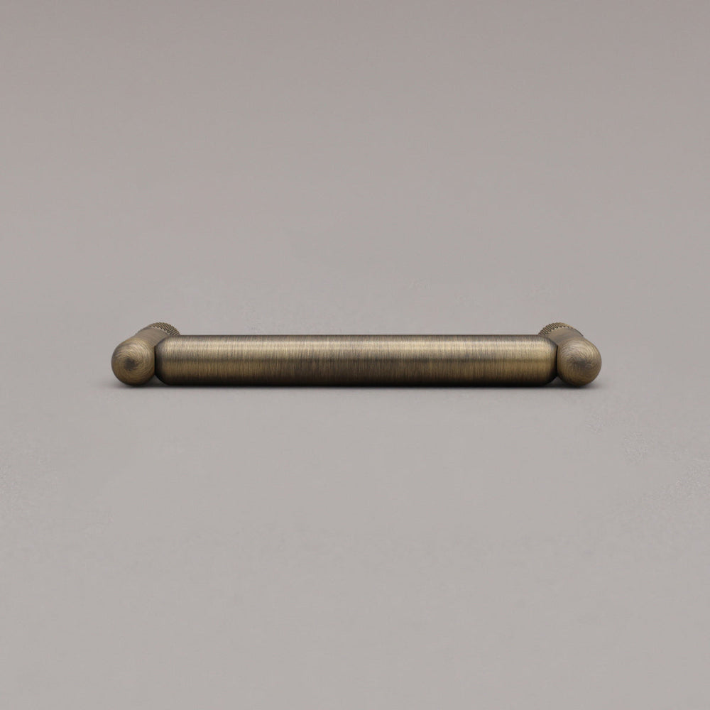smallest knurled pull in aged brass laying down on gray background