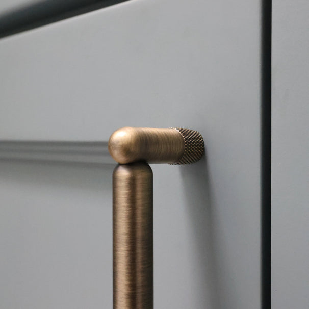 Close up of aged brass knurled pull installed on blue bathroom cabinet