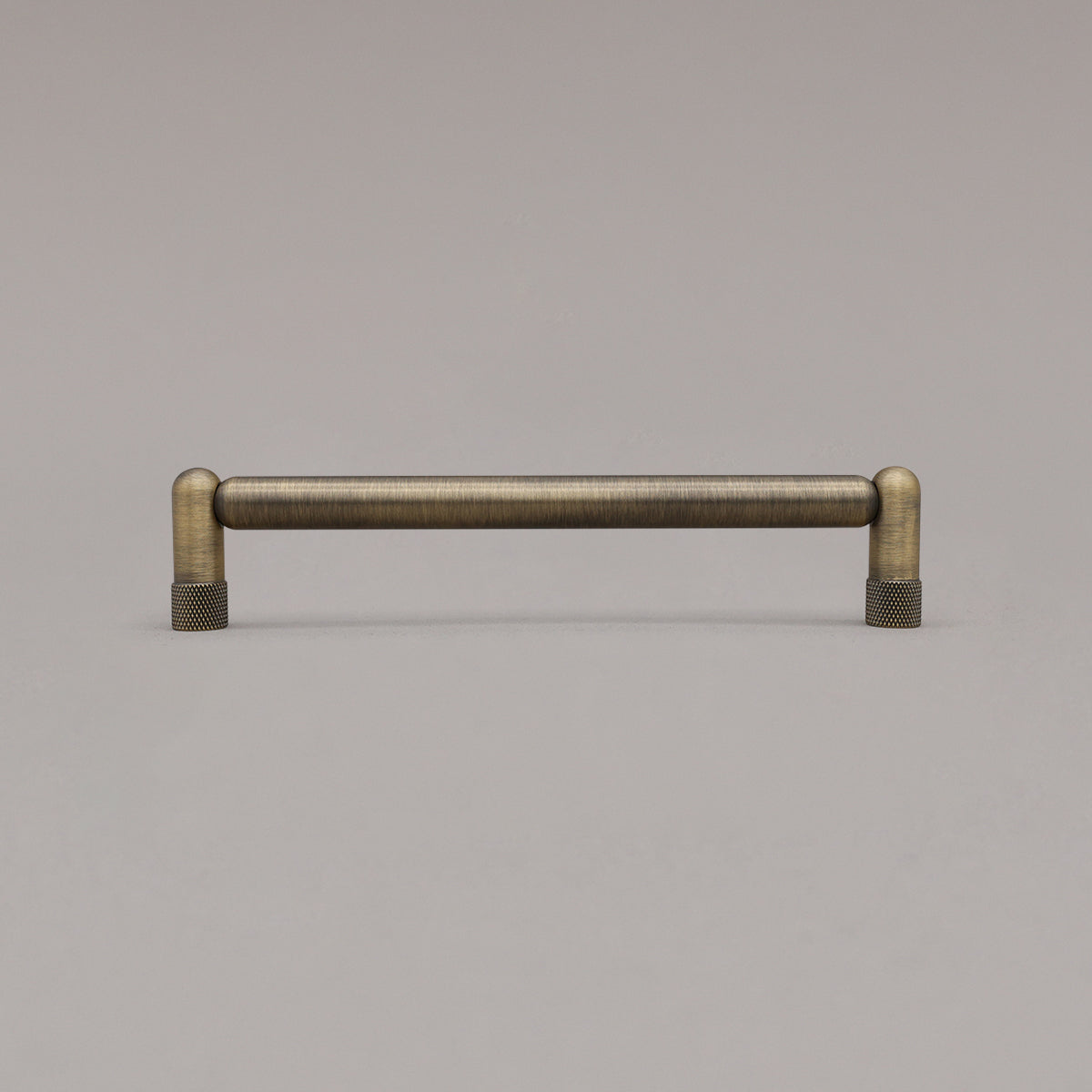 Medium aged brass knurled cabinet pull standing on gray background