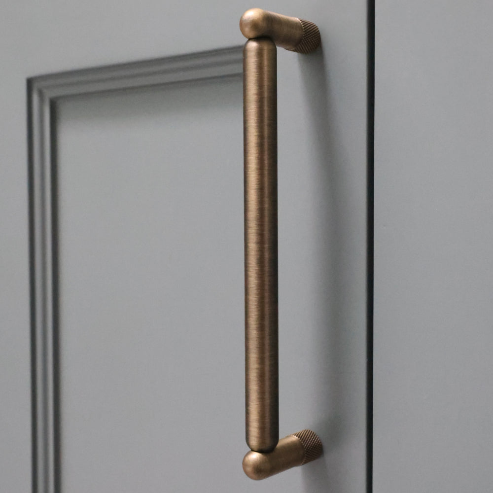 Aged brass knurled cabinet pull installed on blue bathroom cabinet door