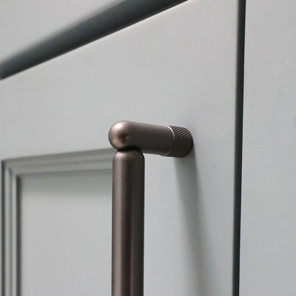 Close up of graphite knurled cabinet pull installed on blue bathroom cabinet door