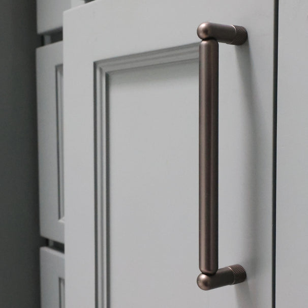 graphite knurled cabinet pull installed on blue bathroom cabinet door