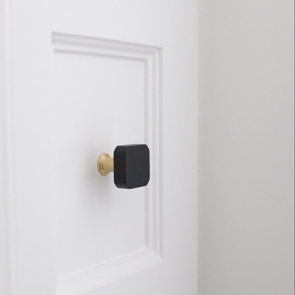 Black and brass gold square knob on a white bathroom drawer