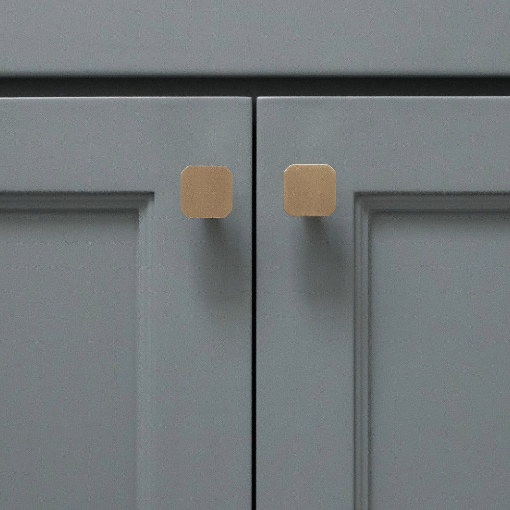 Two gold square knobs installed on blue bathroom cabinet doors