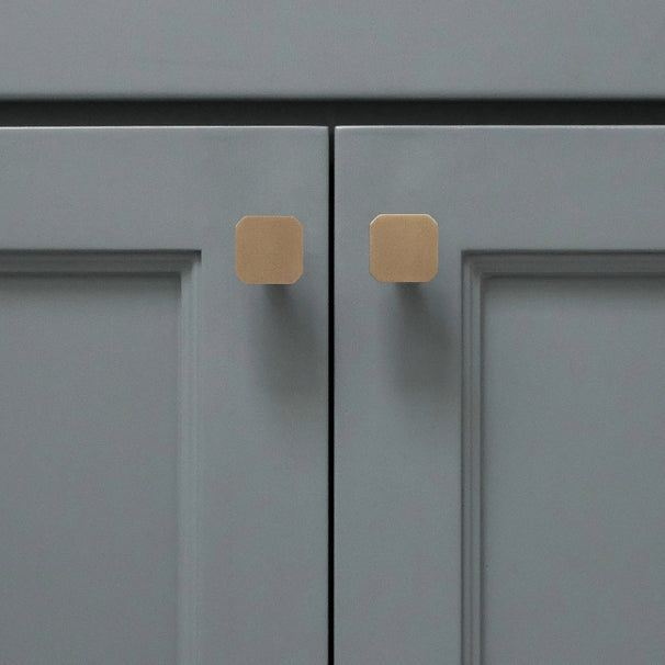 Two gold square knobs installed on blue bathroom cabinet doors