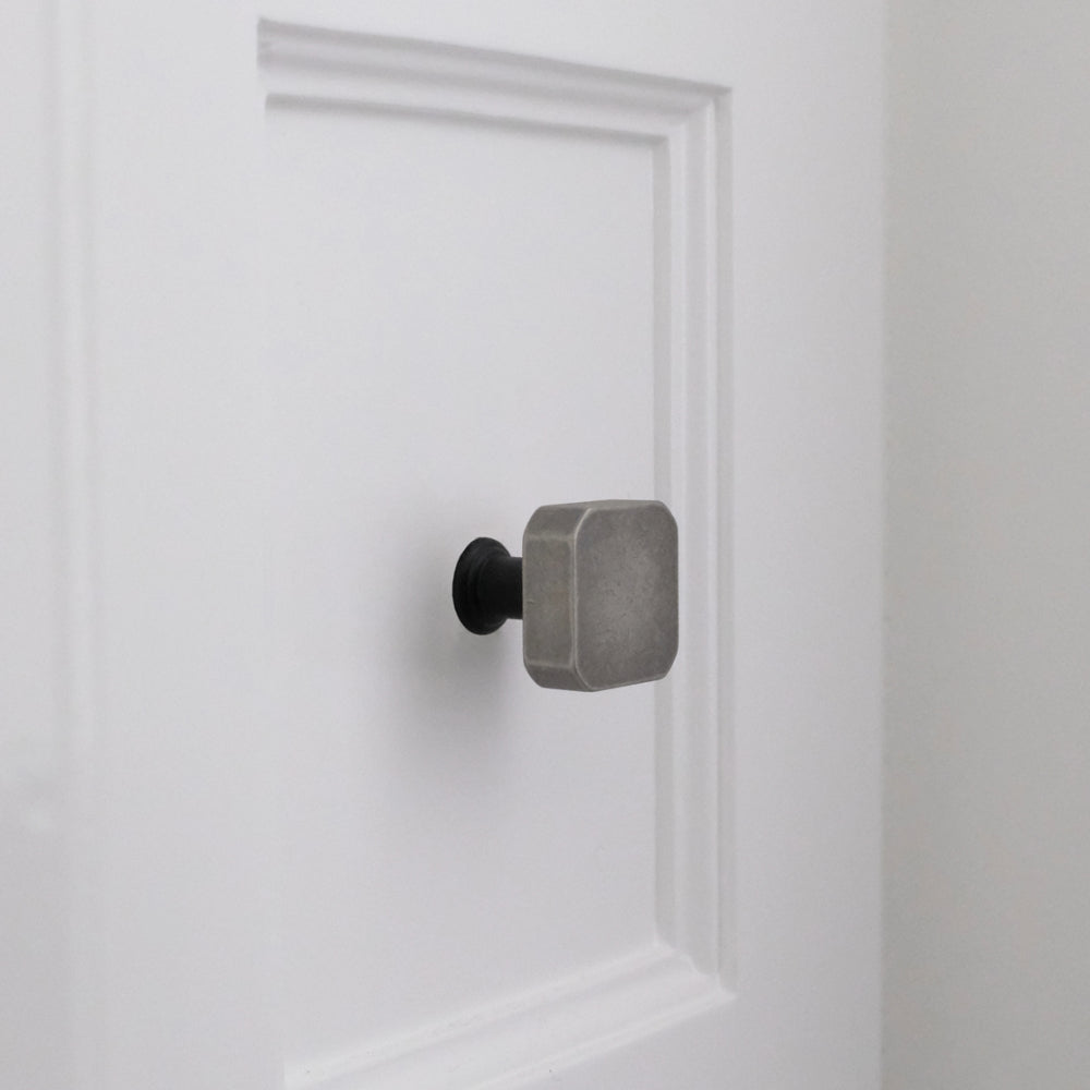 Weathered nickel and matte black two-tone square knob installed on white bathroom cabinet