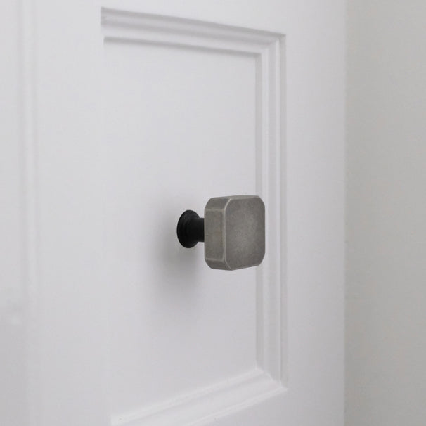 Weathered nickel and matte black two-tone square knob installed on white bathroom cabinet