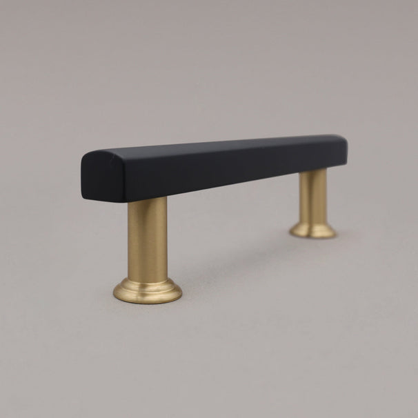 side view of black and brass cabinet pull standing on gray background