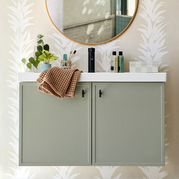 smoke acrylic and matte black stem knobs installed on pale green bathroom vanity cabinet