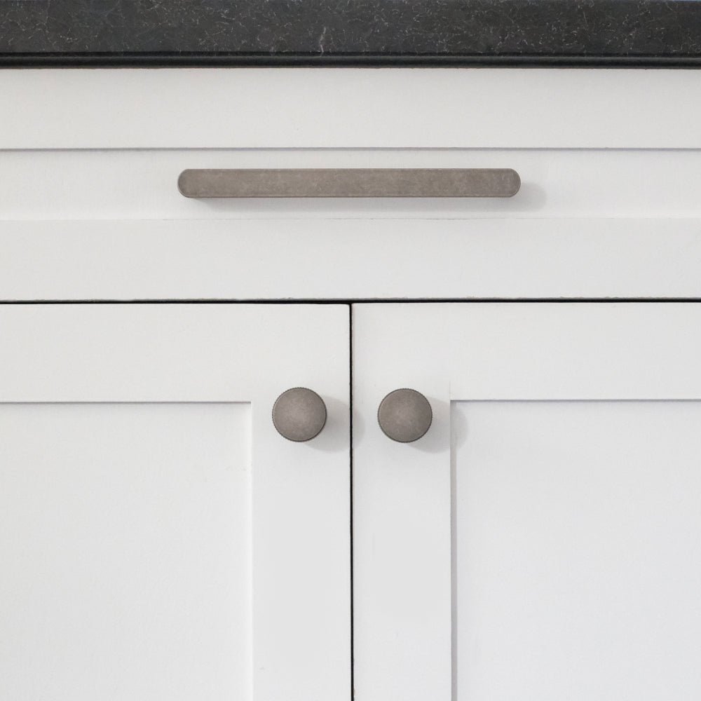 front view of weathered nickel ribbed pull and knobs on white cabinet