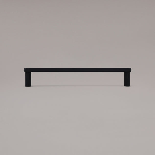 12" Ribbed appliance pull in Matte Black standing on gray background