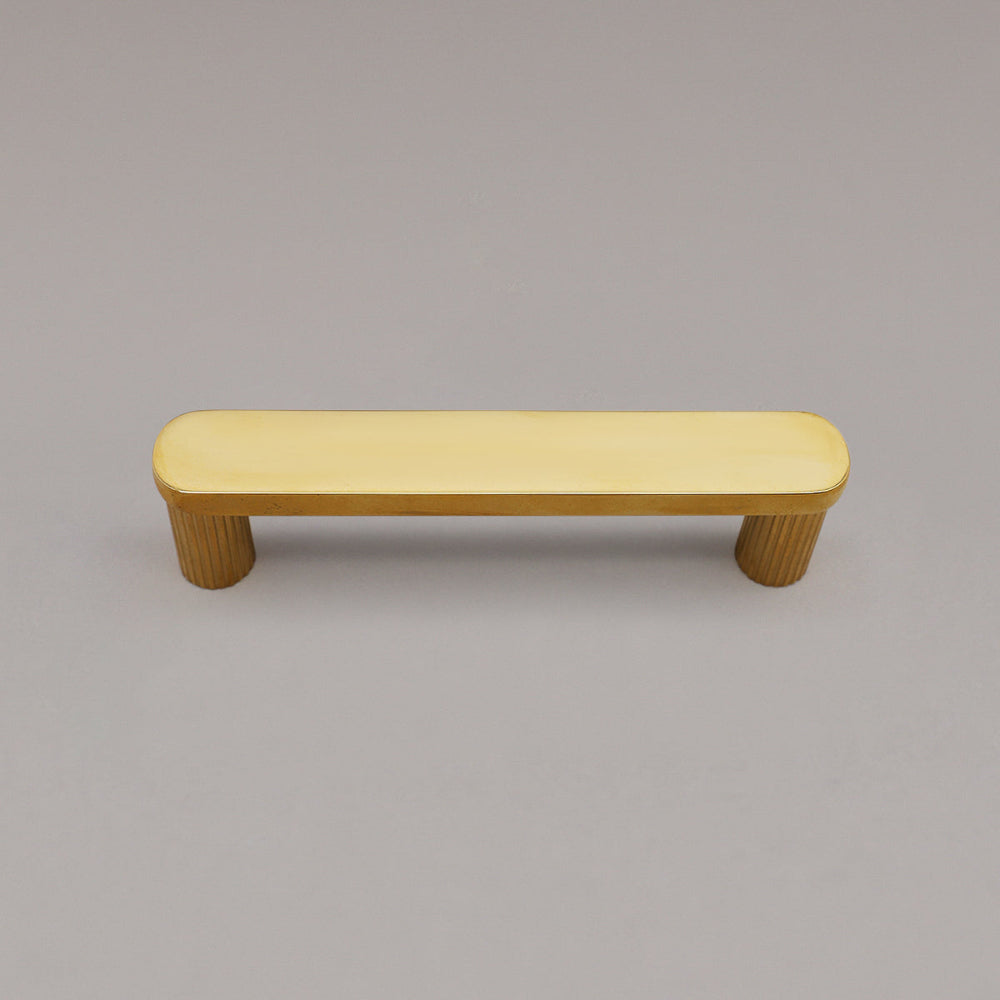 top view of unlacquered polished brass ribbed pull on gray background