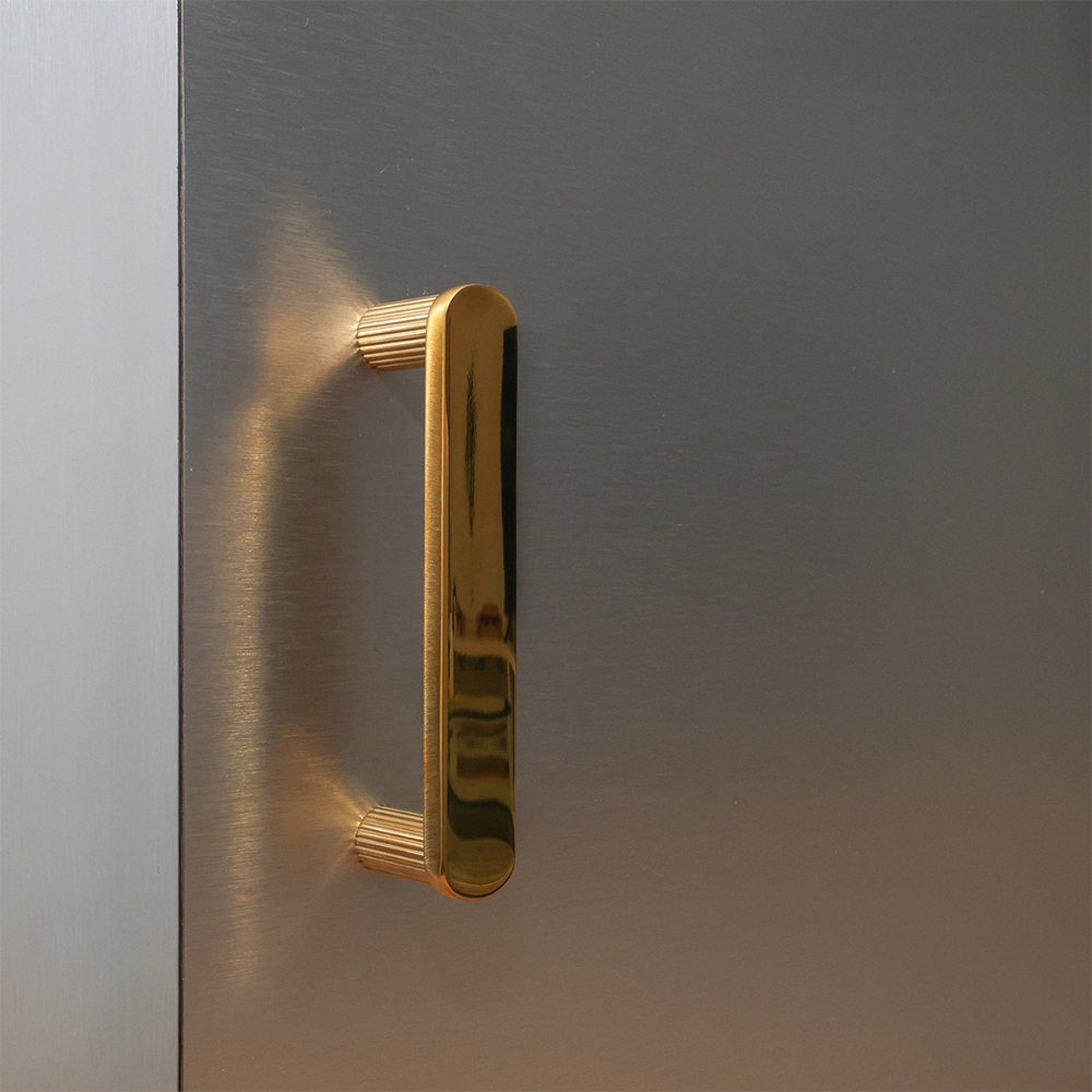 Small ribbed cabinet pull in unlacquered polished brass installed on silver cabinet