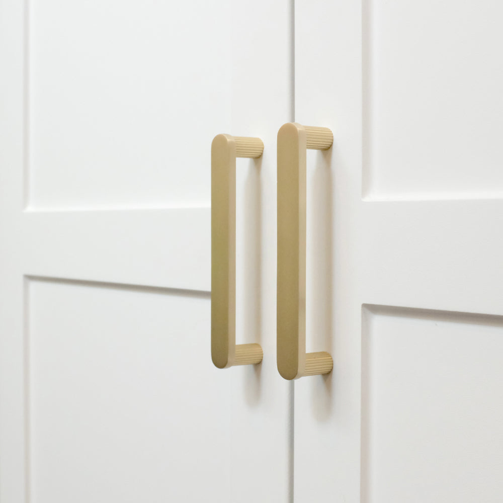 Ribbed satin brass gold cabinet pulls installed on white cabinets