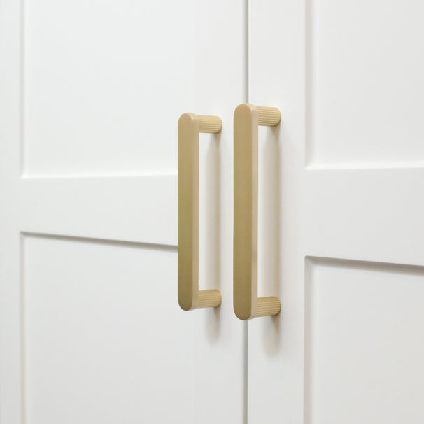 Ribbed satin brass gold cabinet pulls installed on white cabinets