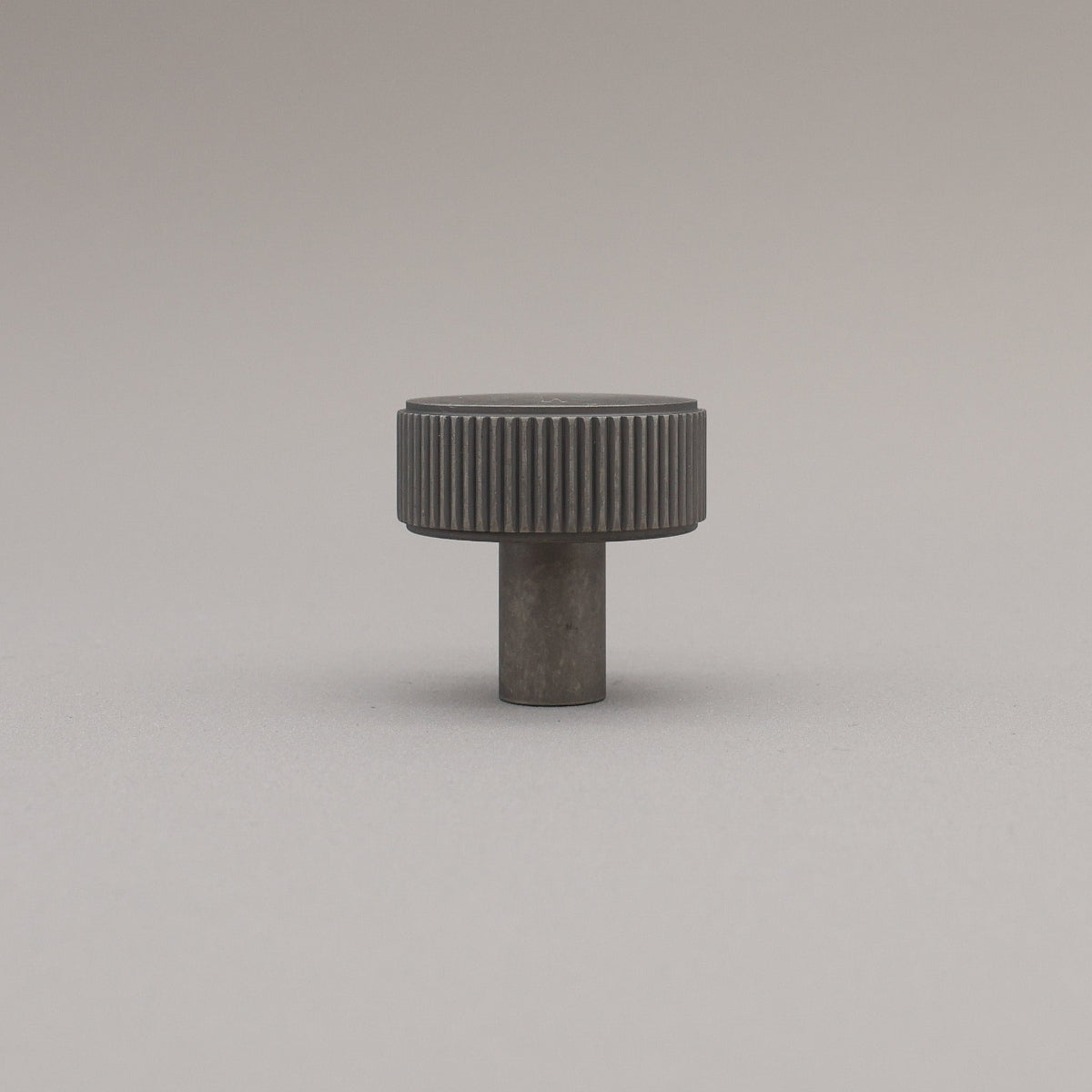 Dark gray cylindrical knob with textured surface on a light gray background