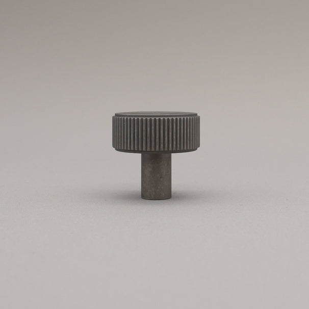 Dark gray cylindrical knob with textured surface on a light gray background