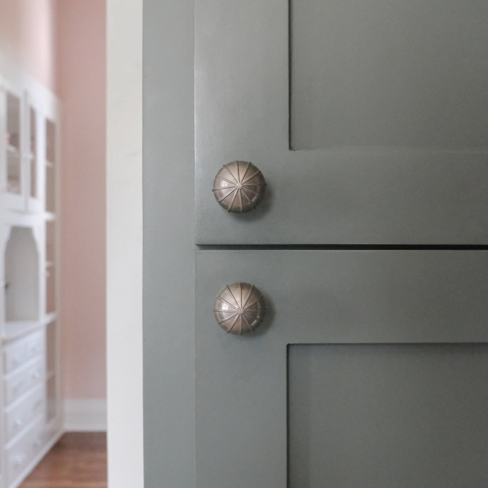 Satin nickel silver sunburst knobs installed on blue kitchen cabinets