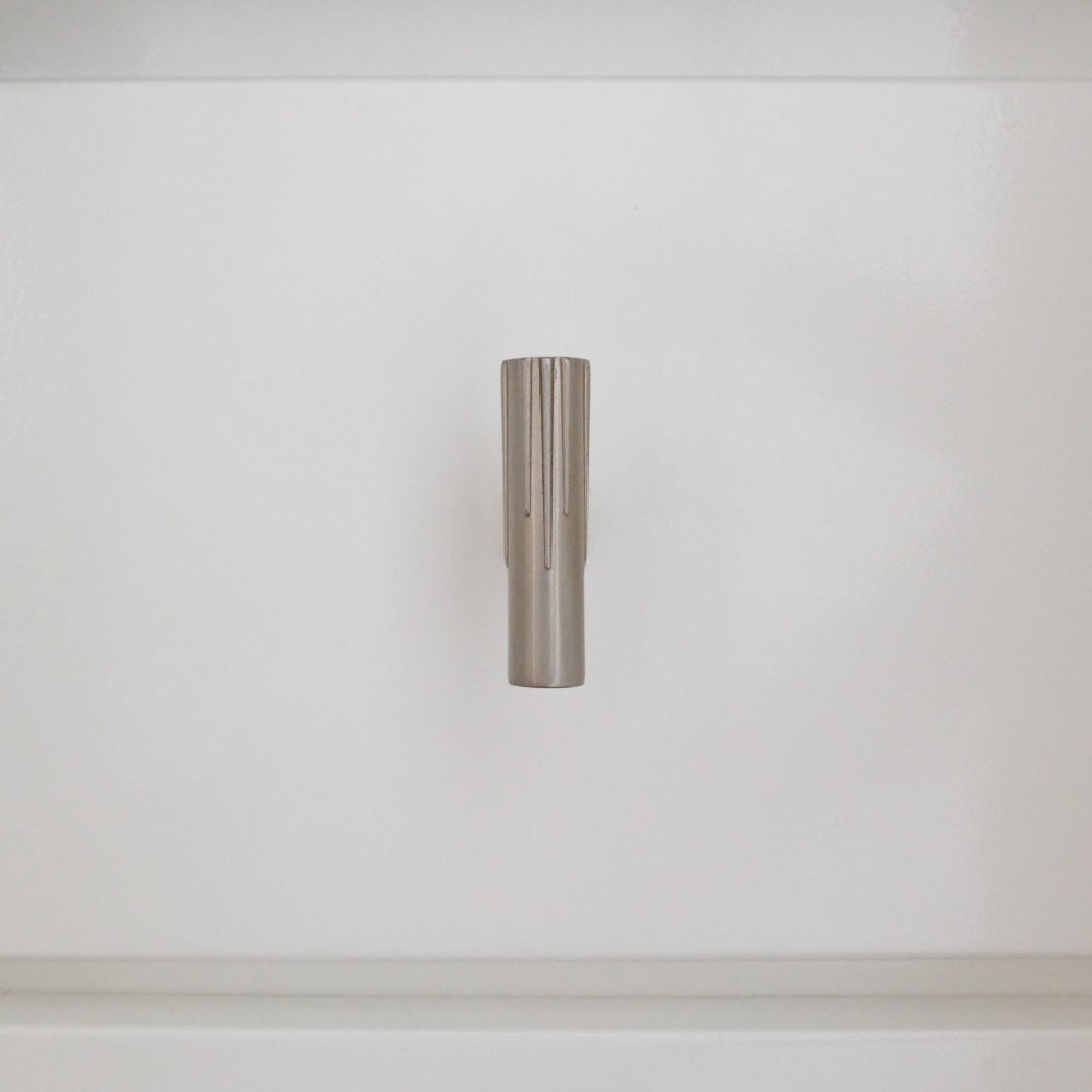 Satin nickel silver t-knob installed vertically on a white bathroom cabinet 