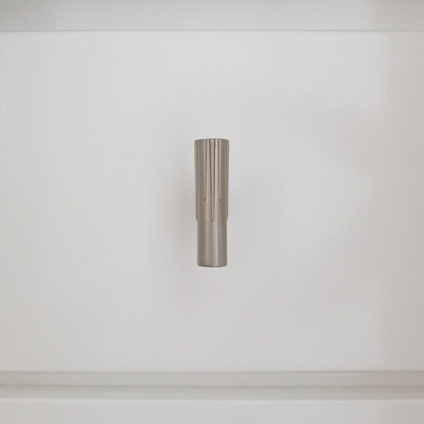 Satin nickel silver t-knob installed vertically on a white bathroom cabinet 
