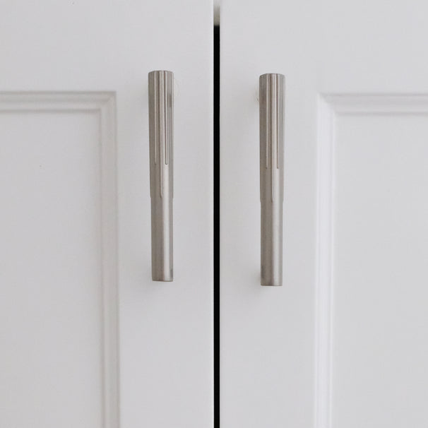 Small silver sunburst satin nickel cabinet pulls installed on white cabinet