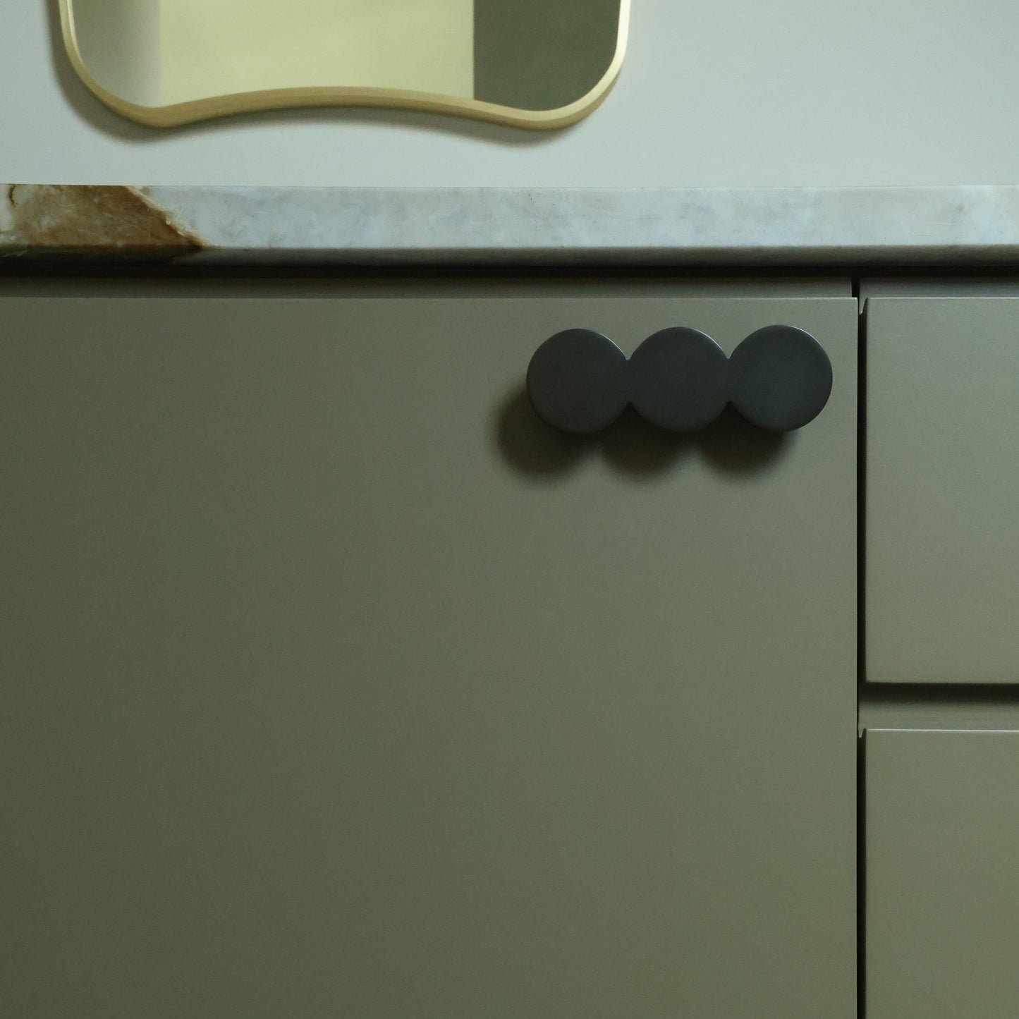 Close-up of a kitchen cabinet with graphite round handles on a light-colored countertop.