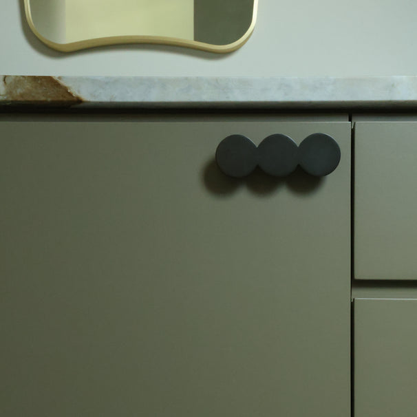 Close-up of a kitchen cabinet with graphite round handles on a light-colored countertop.