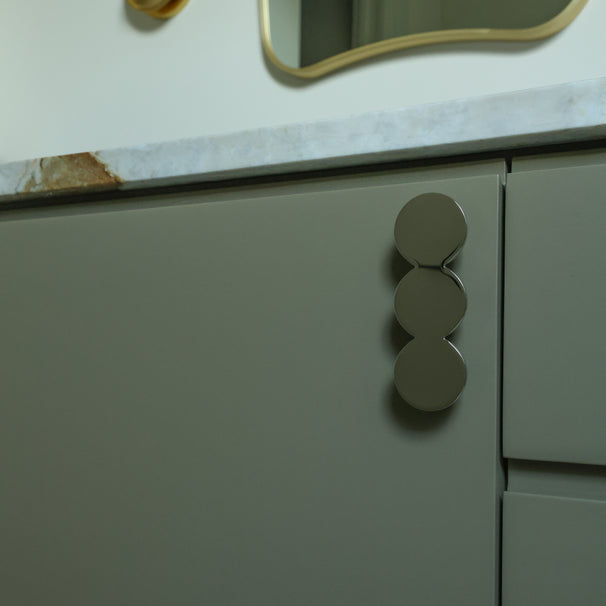 Close-up of a green cabinet with circular handles on a bathroom counter.