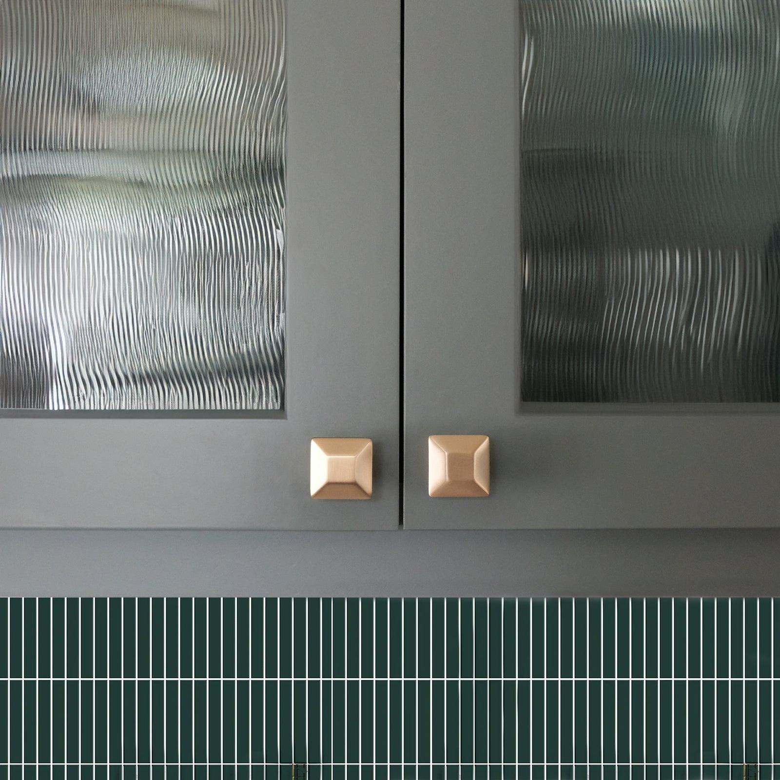 Satin Brass Diamond Cabinet Knobs on Sage Green Cabinets and a Tiled Backsplash.