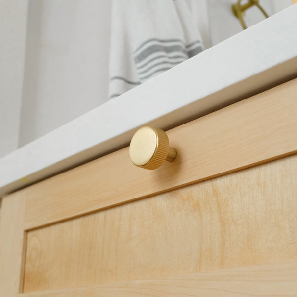Close-up of a wooden cabinet with a gold knob on a neutral background