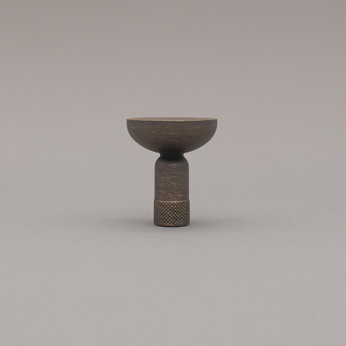 Skinny knurled knob in antique english finish standing upright on grey background. 